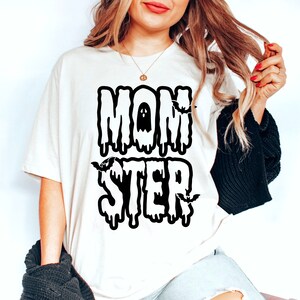 Könnte beinhalten: Weißes T-Shirt mit schwarzem, tropfendem Text, der "MOMSTER" mit einem Geist und Fledermäusen lautet.