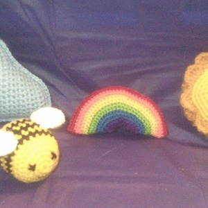 May include: A set of five crocheted stuffed toys: a blue cloud, a rainbow, a yellow sun, and a black and yellow bee.