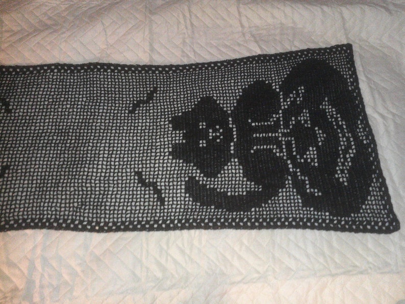 Op de afbeelding: Een zwarte gehaakte tafelloper met een bloemenpatroon. De loper is gemaakt van een fijn, delicaat garen en heeft een kantlook.