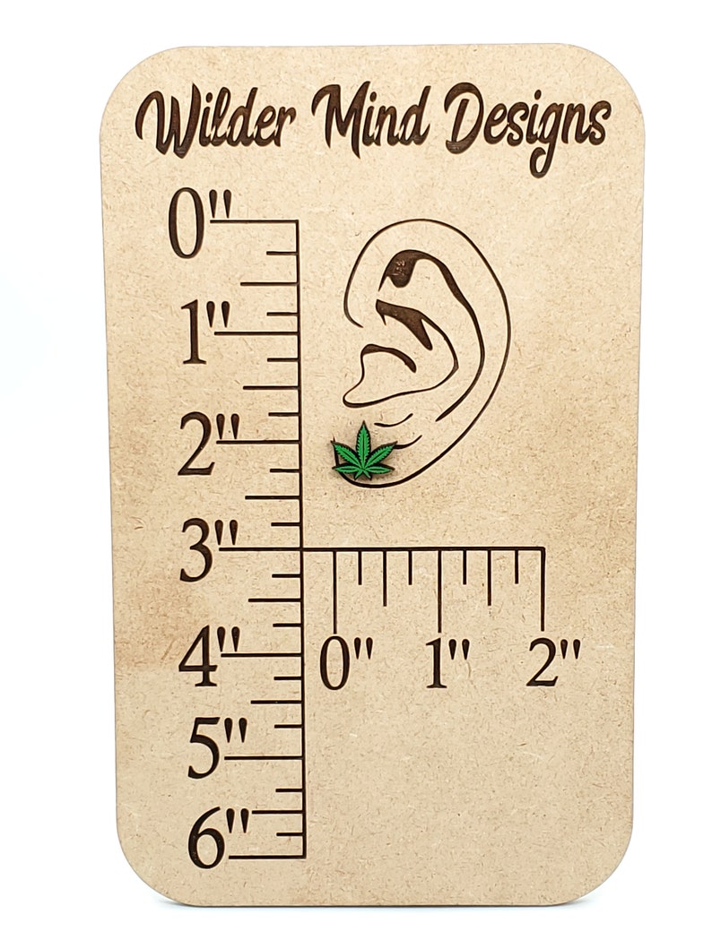 May include: A wooden ruler with a carved ear and a green marijuana leaf earring. The ruler measures up to 6 inches.