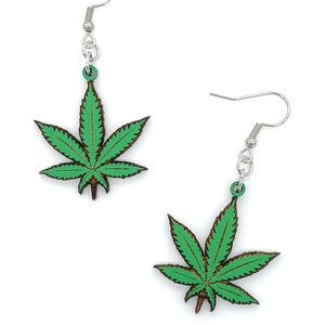 May include: A pair of green marijuana leaf earrings with silver hooks. The leaves are made of wood and have a dark brown outline.