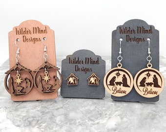 May include: Three sets of wooden Christmas earrings. The first set features a nativity scene with a star on top. The second set features a nativity scene with the words "Believe" on the bottom. The third set features a small nativity scene.
