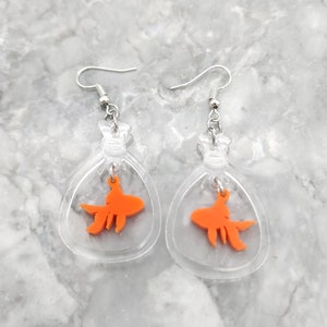 May include: A pair of clear acrylic earrings with a dangling orange goldfish charm inside each earring.