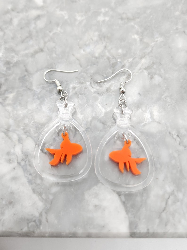 May include: A pair of clear acrylic earrings with a dangling orange goldfish charm inside each earring.