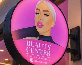 Könnte beinhalten: Ein kreisförmiges, beleuchtetes Außenschild mit schwarzem Rahmen, das an einer Wand montiert ist. Das Schild zeigt eine grafische Illustration einer Person mit blondem Haar und pinkem Lippenstift vor einem leuchtend pinken Hintergrund, mit dem Text BEAUTY CENTER, BEAUTY & CONFIDENCE und dem Instagram-Handle beauty.center.