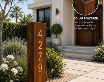 Könnte beinhalten: Ein hohes, rechteckiges Hausnummernschild aus rostfarbenem Metall mit den vertikal angeordneten Ziffern 4279. An der Oberseite befindet sich ein Solarpanel mit dem Text SOLAR POWERED, das tagsüber Energie speichert und nachts für Beleuchtung sorgt.