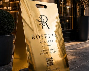 Könnte beinhalten: Ein goldfarbenes A-förmiges Gehwegaufsteller-Schild mit reflektierender Oberfläche. Das Schild zeigt den schwarzen Text Rosetta Atelier, ein Logo mit einem Buchstaben R und Blattmotiv, den Satz Timeless Style Curated For You, einen QR-Code.