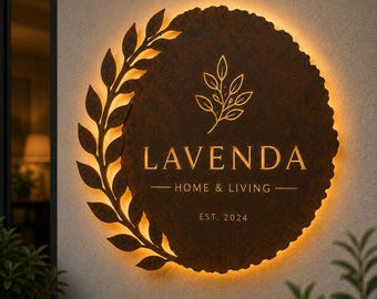 Könnte beinhalten: Ein kreisförmiges, dunkles, strukturiertes Metall-Wandschild mit Hintergrundbeleuchtung. Es zeigt ein Blattzweig-Design auf der linken Seite, ein zentrales Zweig-Symbol und den Text "LAVENDA HOME & LIVING EST. 2024" in goldener Schrift.