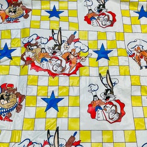 May include: A white sheet with a yellow and white checkered pattern, featuring cartoon characters like Bugs Bunny, Daffy Duck, and the Tasmanian Devil in chef attire, along with blue stars.