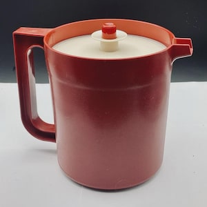 May include: A vintage red plastic pitcher with a matching handle and lid. The pitcher has a white lid with a red and white knob. The pitcher is designed for serving beverages and has a spout for easy pouring.