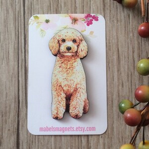 Puede incluir: Un imán de madera con un perro caniche marrón y blanco. El imán está en una tarjeta blanca con flores rosas y el texto "mabelsmagnets.etsy.com".