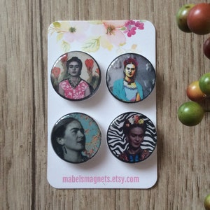 May include: Set of four round magnets featuring images of Frida Kahlo. Each magnet has a different image of Frida Kahlo, including one with a floral background, one with a blue background, one with a blue and green background, and one with a zebra print background. The magnets are on a white card with the text "mabelsmagnets.etsy.com".