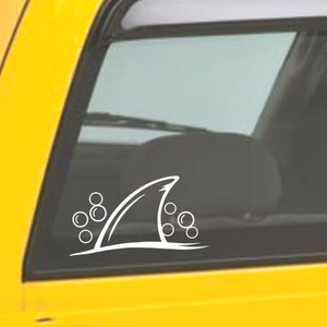 May include: White vinyl decal of a shark fin with bubbles, suitable for car windows or other smooth surfaces.