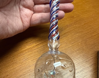 Könnte beinhalten: Eine durchsichtige Glasglocke mit einem rot-weiß-blauen gedrehten Griff und einer roten Kugel an der Spitze. Die Glocke hat ein florales Design und einen kleinen Kristall im Inneren.