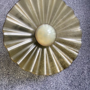 May include: A round, gold-colored ceiling light fixture with a frosted glass shade. The shade has a scalloped edge and a central dome.