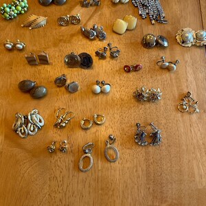 May include: A collection of vintage earrings in various styles and colours, including gold, silver, and pearl. The earrings are displayed on a wooden surface.