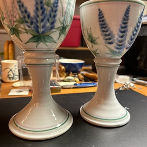 May include: Two white ceramic cups with blue and green floral designs. The cups have a stem and a wide base.