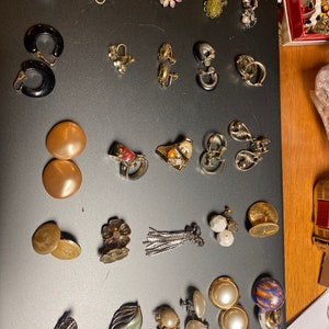 May include: A collection of vintage earrings in various styles and colours, including gold, silver, black, white, and green. The earrings feature a variety of designs, such as flowers, leaves, and geometric shapes.