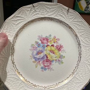May include: White ceramic plate with a gold rim and a floral design in shades of pink, yellow, blue, and green.