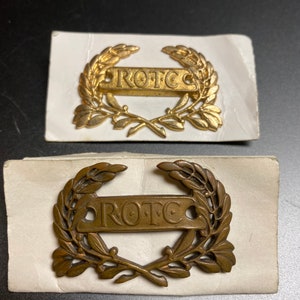 May include: Two gold-colored ROTC pins with a laurel wreath design. The pins are on white card stock.