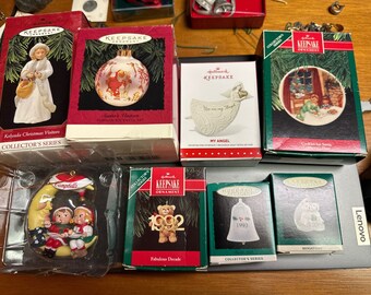 May include: A collection of Hallmark Keepsake Christmas ornaments in their original boxes. The ornaments feature various designs, including angels, bells, and characters. Some boxes have text such as "My Angel" and "1992 Fabulous Decade."