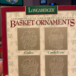 May include: A set of four Longaberger commemorative Christmas basket ornaments. The ornaments are decorated with a cookie, candy cane, mistletoe, and poinsettia.