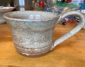 May include: A speckled brown and white ceramic mug with a rounded handle. The mug has a speckled glaze and a brown rim.