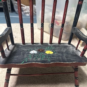 May include: A small wooden chair painted black with red accents. The chair has a painted floral design on the seat.