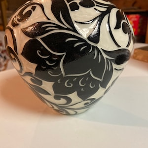 May include: A white ceramic vase with a black floral design. The vase has a round body and a narrow neck.