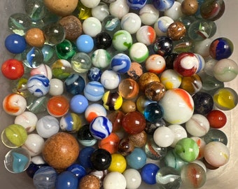 May include: A collection of colorful glass marbles in a clear plastic container. The marbles are various sizes and colors, including blue, red, green, yellow, white, and brown. Some of the marbles have swirls or patterns.