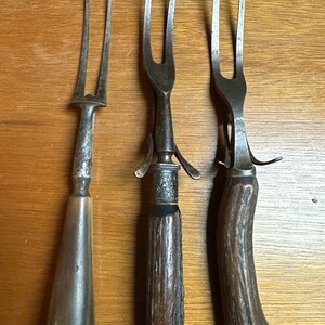 以下が含まれることがあります： 木製のハンドルが付いたアンティークの銀製のフォーク3本。フォークは2本の先端があり、食べ物を盛り付けるために作られています。ハンドルは濃い木でできており、自然な仕上げになっています。