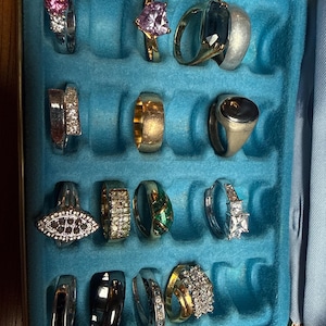 Op de afbeelding: Een verzameling diverse ringen tentoongesteld in een blauwe sieradendoos. De ringen hebben verschillende ontwerpen, waaronder edelstenen, diamanten en uniek metaalwerk. De ringen zijn in zilver- en goudtinten.
