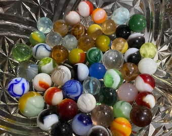May include: A collection of colorful glass marbles in a clear glass bowl. The marbles are various sizes and colors, including red, blue, green, yellow, white, and black.