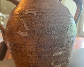 May include: A brown ceramic pitcher with two handles. The pitcher has white lettering that reads "First the Word, then the Song, of God".