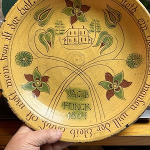 Könnte beinhalten: Ein gelber Keramikteller mit einem braunen, grünen und weißen Blumendesign. Der Teller hat eine handschriftliche Inschrift in Deutsch, die lautet "In der Schüssel steth ein..." und "Jacob Funck 1804".