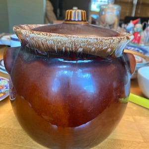May include: A brown ceramic crock pot with a lid. The lid has a white glaze with brown speckles. The crock pot is glazed in a brown color.