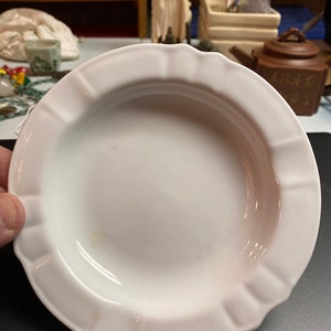 Puede incluir: Un cenicero de cerámica blanca con un borde acanalado. El cenicero es redondo y tiene un pozo poco profundo en el centro.