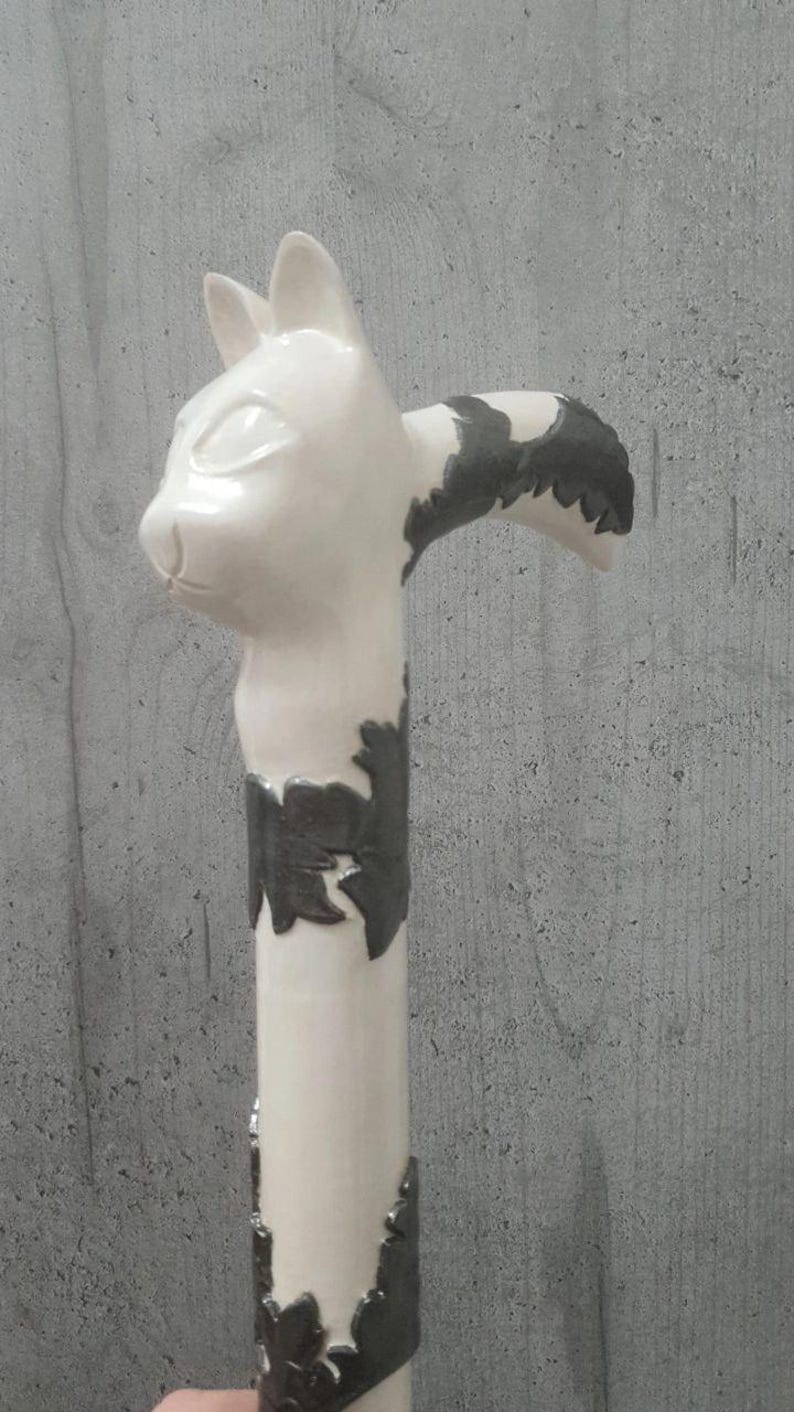 Pu&ograve; includere: Bastone in ceramica bianca con manico a forma di testa di gatto. Il volto del gatto &egrave; dettagliato con occhi e orecchie. L'asta del bastone presenta decorazioni nere. Il bastone &egrave; alto circa 91 cm.