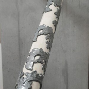 Pu&ograve; includere: Un bastone bianco con un'impugnatura curva e disegni argentati di rami d'albero che avvolgono l'asta. Il bastone &egrave; un oggetto decorativo, forse per la moda o il supporto.