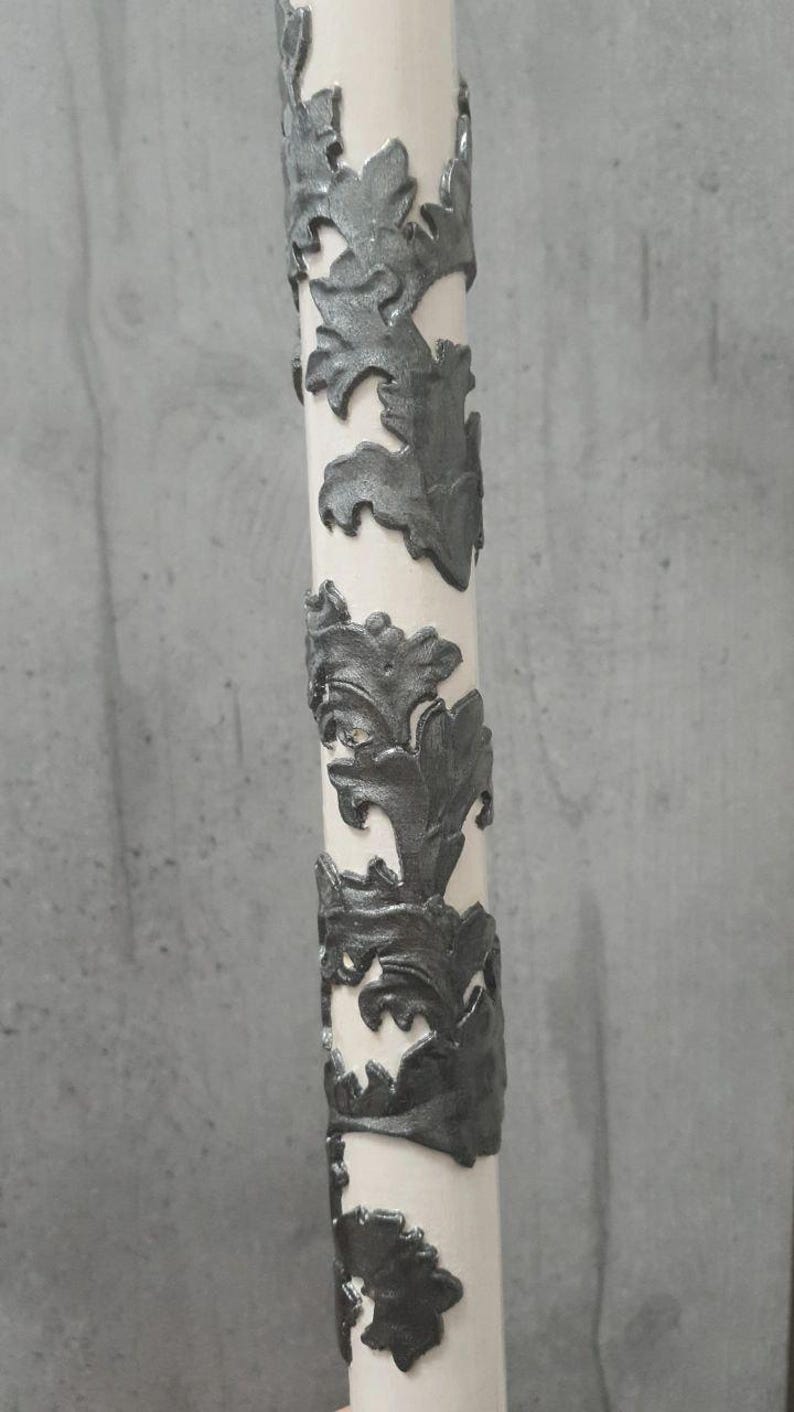 Pu&ograve; includere: Un oggetto decorativo cilindrico bianco con motivi a forma di foglia grigio scuro che avvolgono la sua superficie. Il design &egrave; in rilievo, creando un aspetto strutturato. L'oggetto &egrave; posto su uno sfondo grigio neutro.