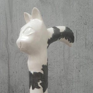 Pu&ograve; includere: Un bastone in ceramica bianca a forma di gatto con dettagli neri. La testa del gatto &egrave; in cima, con orecchie e un viso dettagliato. Il corpo del bastone presenta motivi neri irregolari. Il design &egrave; stravagante e decorativo.