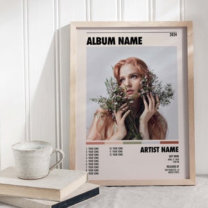 May include: A framed album cover with a woman with red hair holding flowers. The album cover is titled "ALBUM NAME" and features the artist name "ARTIST NAME". The album was released in 2024.