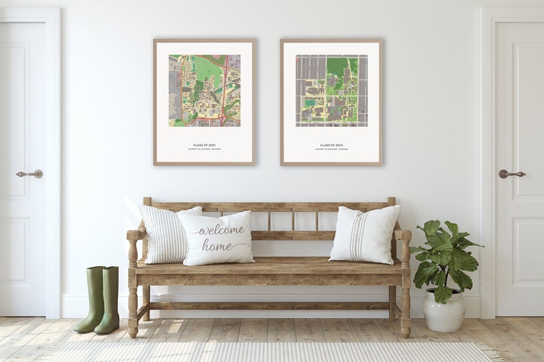 May include: Two framed maps of a university campus, with the text "Class of 2023" and "Class of 2024" below each map. The maps are hanging on a white wall above a wooden bench with pillows. A green plant is in a white pot on the right side of the image.