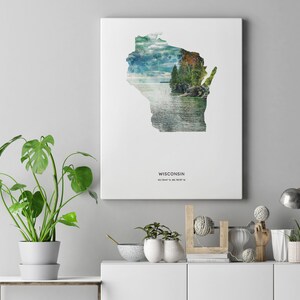 May include: A white canvas print featuring a watercolor illustration of the state of Wisconsin with a scenic lake and forest scene. The print includes the text "WISCONSIN" and the coordinates "43.0747&deg; N, 89.3844&deg; W".
