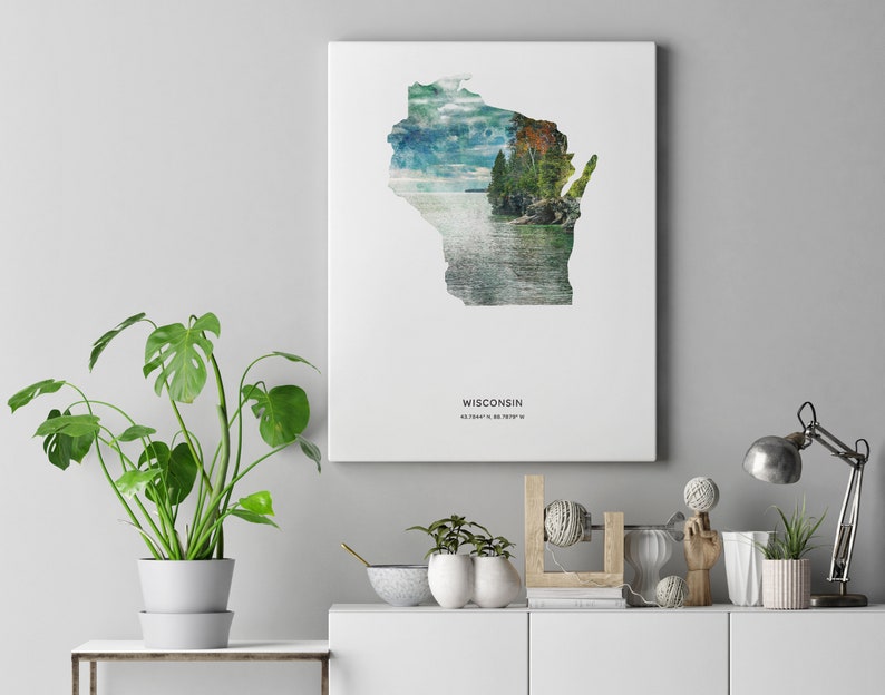 May include: A white canvas print featuring a watercolor illustration of the state of Wisconsin with a scenic lake and forest scene. The print includes the text "WISCONSIN" and the coordinates "43.0747&deg; N, 89.3844&deg; W".