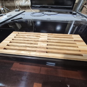 May include: A rectangular wooden cutting board with a light brown finish. The board features a series of parallel, evenly spaced grooves, creating a unique design. The wood grain is visible, adding to its natural aesthetic. This kitchen item is ideal for food preparation.
