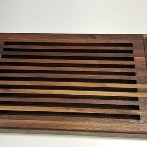 May include: A rectangular wooden cutting board with a slatted design. The board is made of dark brown wood and has a natural finish.