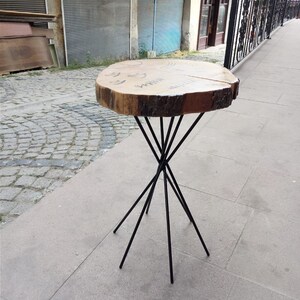 Puede incluir: Una mesa de madera con un borde natural y patas de metal negro. La mesa es de color marr&oacute;n claro y redonda. Las patas son delgadas y se extienden desde el centro de la mesa.