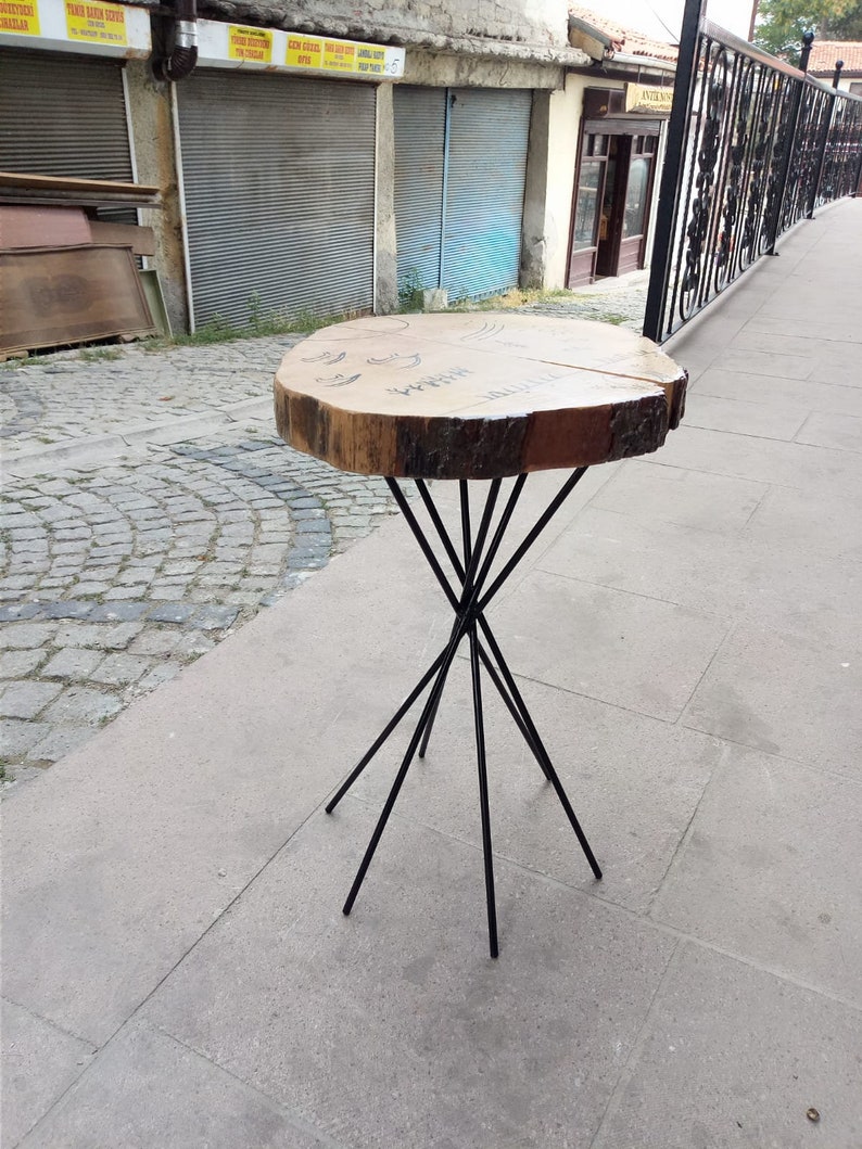 Puede incluir: Una mesa de madera con un borde natural y patas de metal negro. La mesa es de color marr&oacute;n claro y redonda. Las patas son delgadas y se extienden desde el centro de la mesa.