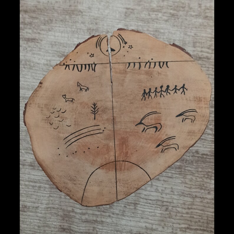 Puede incluir: Un disco de madera con dibujos de animales, estrellas y personas hechos con tinta negra. El disco est&aacute; dividido en dos mitades con una l&iacute;nea en el medio. Los dibujos del lado izquierdo incluyen un ciervo, un &aacute;rbol y una serie de l&iacute;neas. Los dibujos del lado derecho incluyen un grupo de personas caminando, una serie de animales con cuernos y estrellas.